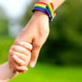 Hand mit Regenbogenarmband hält Kinderhand